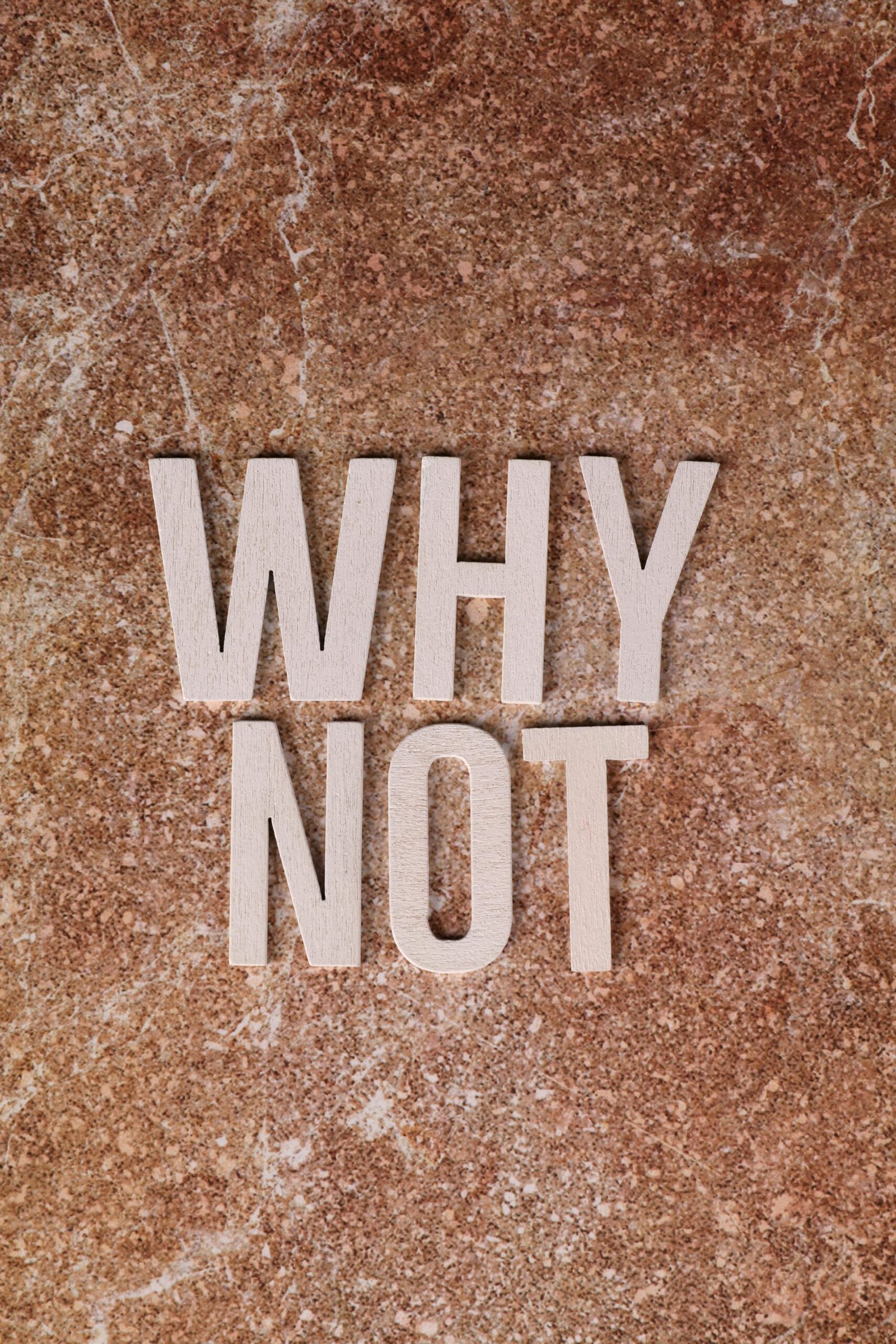 Inspiring 'Why Not' message in wooden letters on marbled surface.